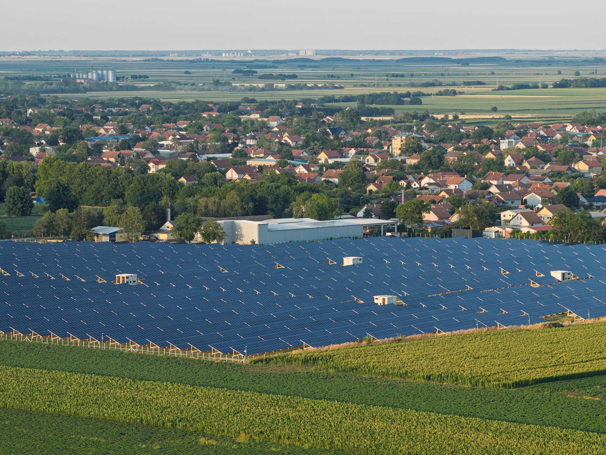 Aerial view of a solar panel field next to a village surrounded by green meadows: a step towards clean electricity for all.