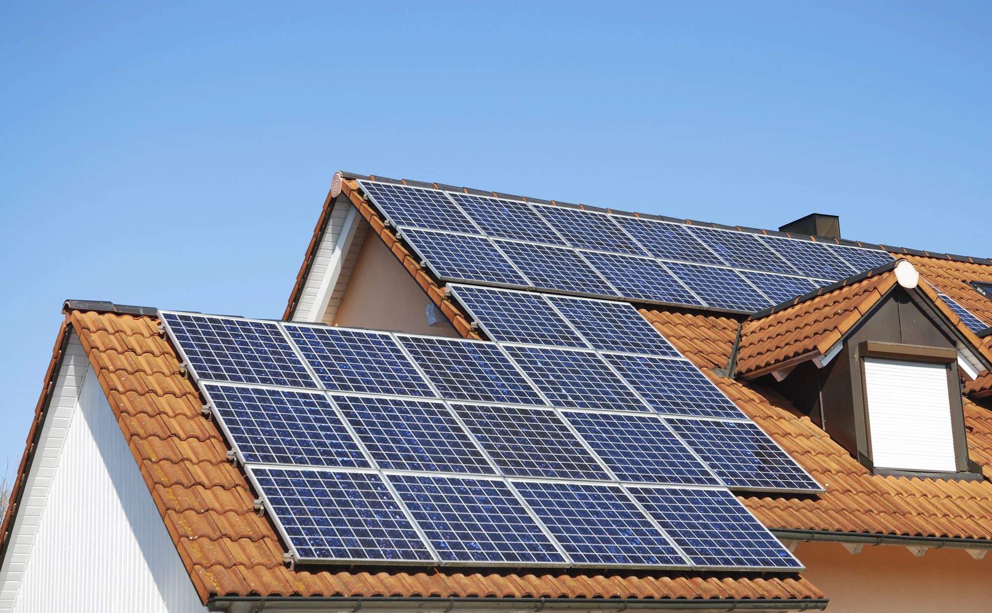 A house roof with solar panels under a clear blue sky.